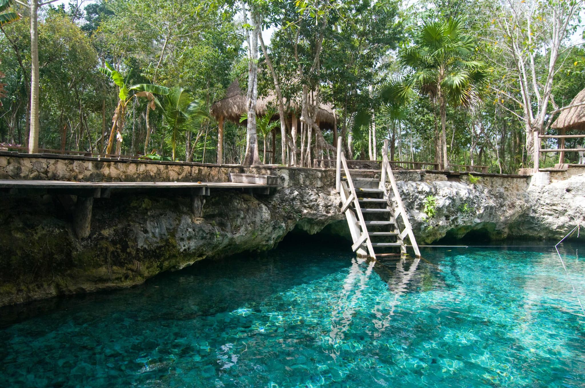 Cenote de agua turquesa con escalera de madera cerca de Tulum