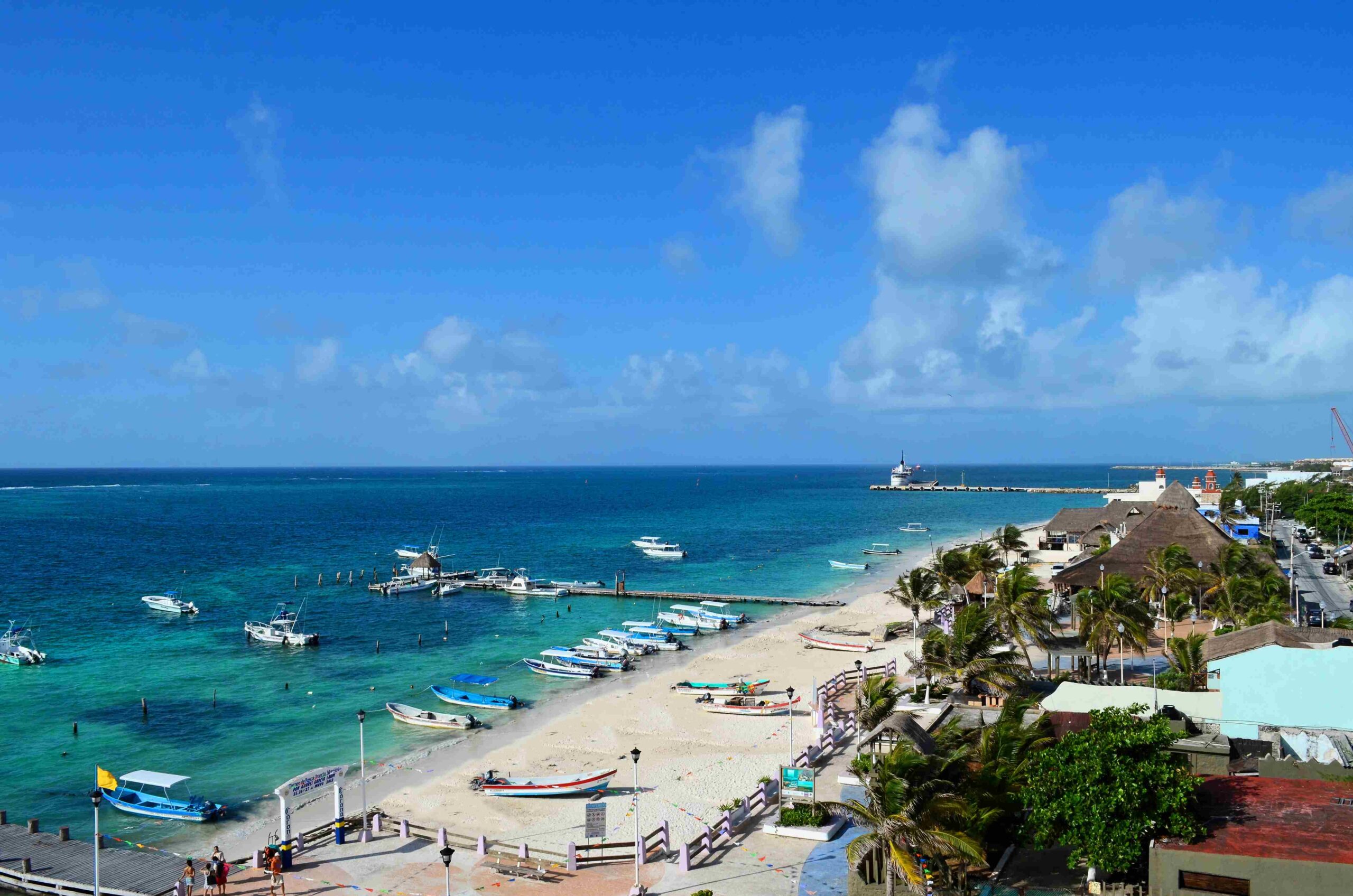 Playa de Puerto Morelos vista desde arriba, con lanchas en la orilla, palmeras y el muelle al fondo