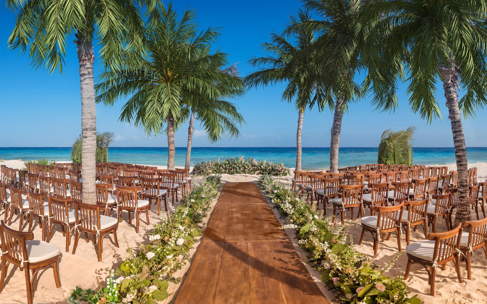 Montaje de una ceremonia de boda en la playa, con sillas de madera, flores y palmeras frente al mar Caribe